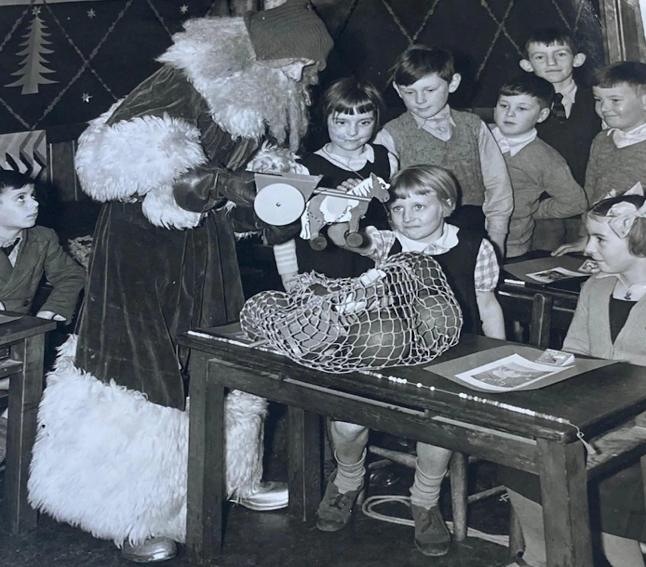 children with father christmas and a wooden horse and cart and a bag of presents.