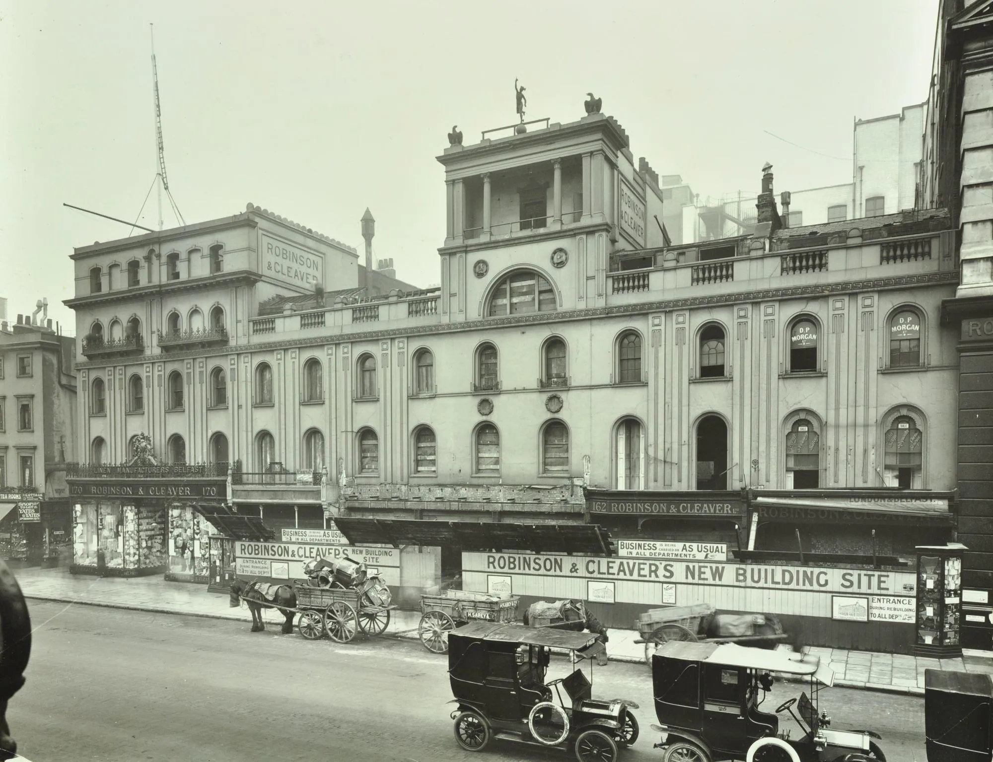 building works commencing with a horse and cart and two early motor cars in the foreground